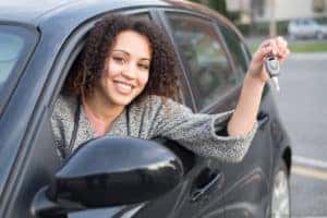A woman is holding car keys outside of her vehicle window.