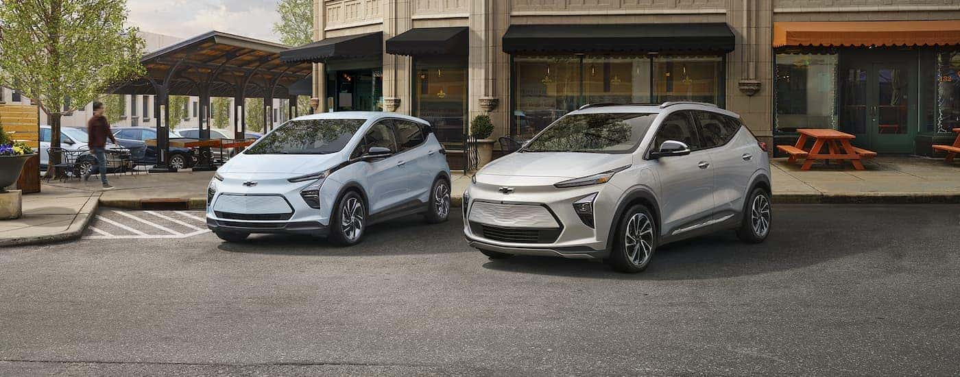 A light blue 2023 Chevy Bolt EV and grey EUV are shown parked on a city street. 