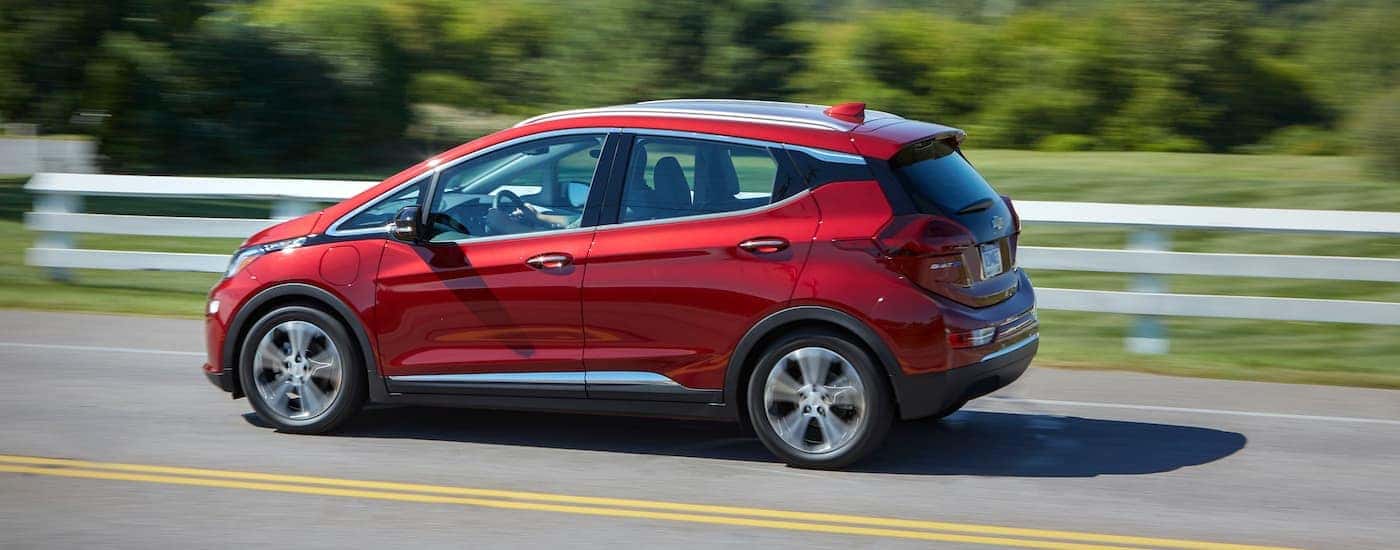 A red 2019 Chevy Bolt EV is shown from the side driving next past a white fence.