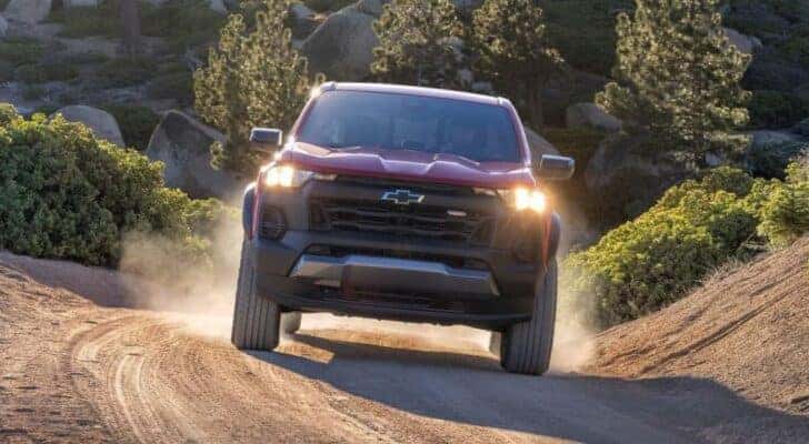 A red 2023 Chevy Colorado Trail Boss is shown from the front driving on a dusty trail.