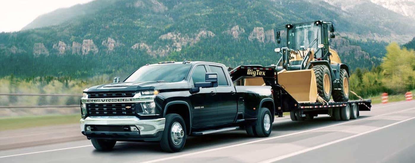 A black 2020 Chevy Silverado 3500 HD is shown from the front at an angle while towing a loader after leaving a dealer that has used Chevy trucks for sale.