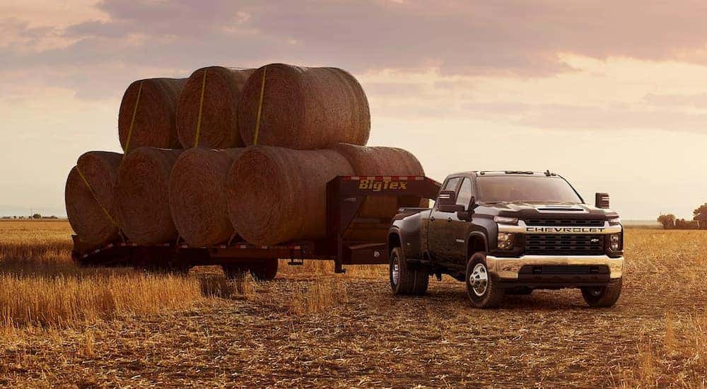 A black 2023 Chevy Silverado 3500 HD is shown from the front at an angle while hauling hay on a trailer.