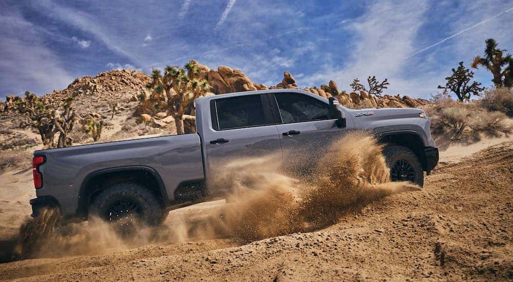 A grey 2024 Chevy Silverado 2500 ZR2 is shown from the side while driving through sand.