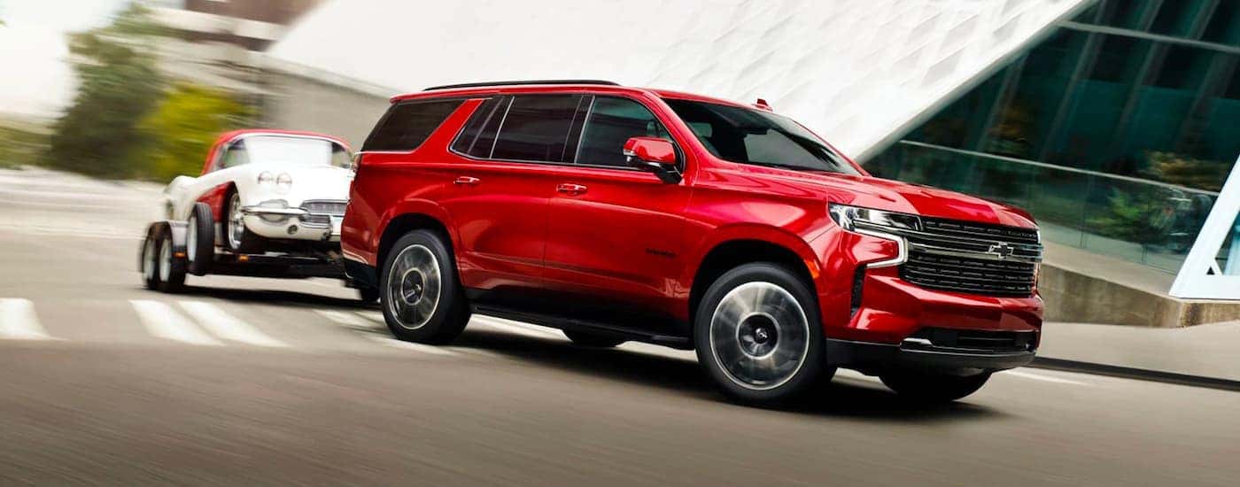 A red 2023 Chevy Tahoe is shown towing a show car.