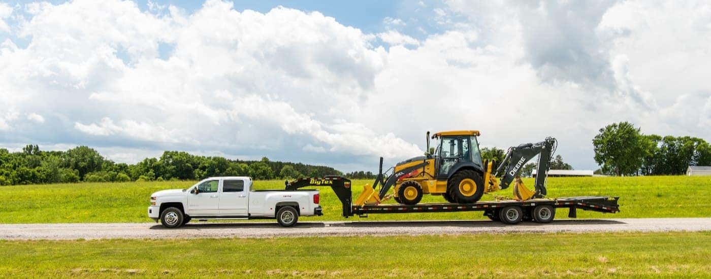 A white 2019 Chevy Silverado 3500HD is towing heavy machinery after leaving Swartz.