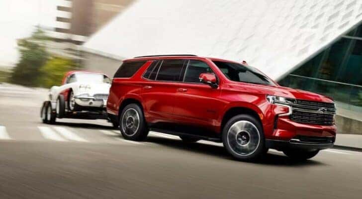 A red 2023 Chevy Tahoe is shown towing a car after viewing a used Chevy Tahoe for sale.