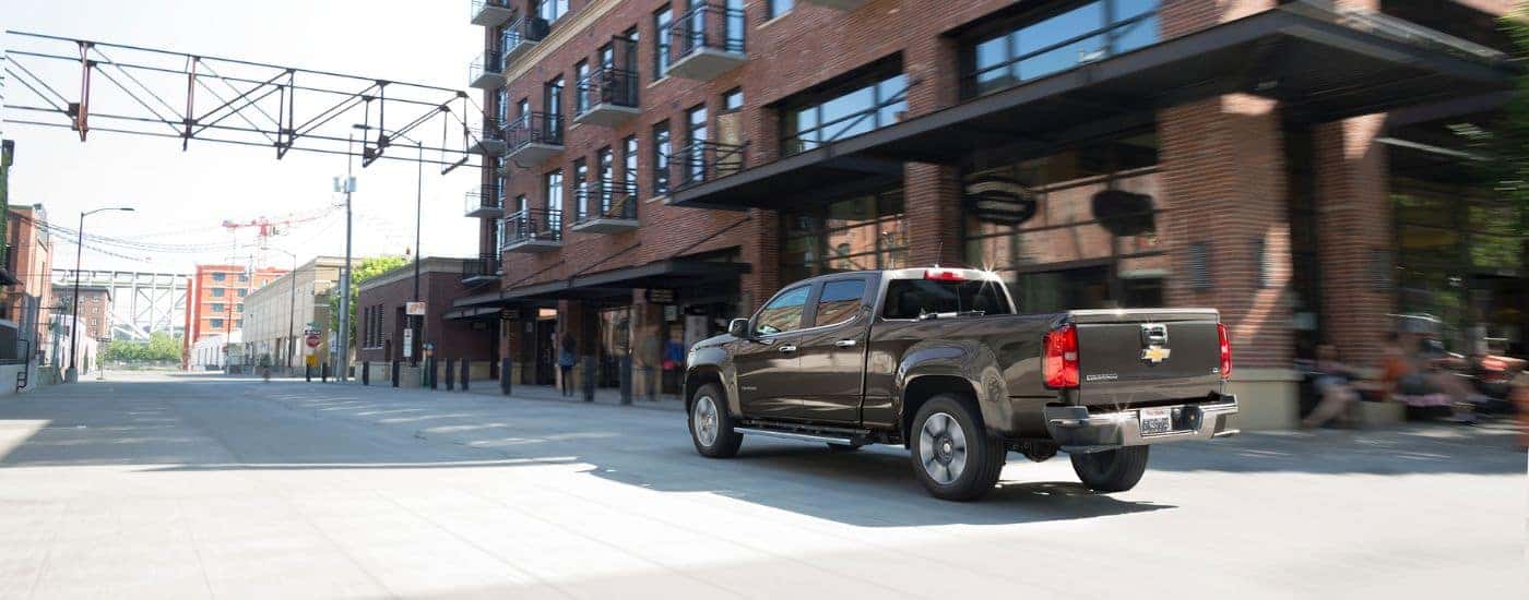 A black 2015 used Chevy Colorado for sale is shown driving on a city street.