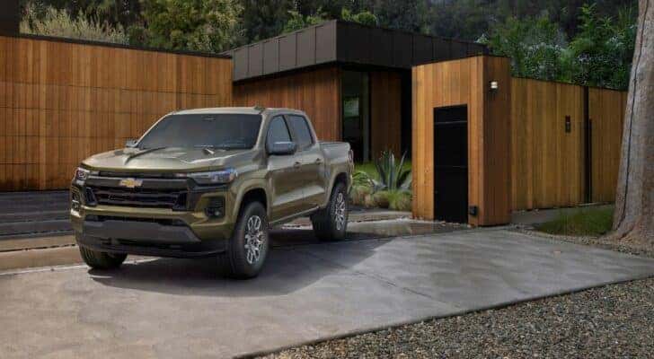 A green 2023 Chevy Colorado LT is shown on the driveway of a modern house.