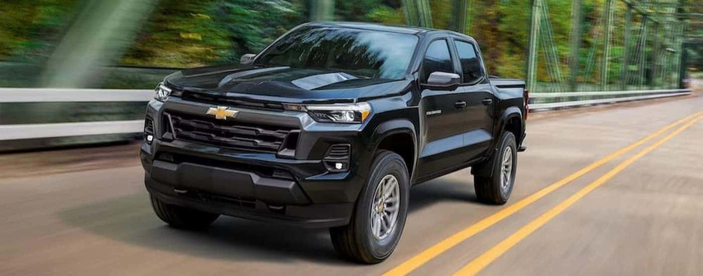 A black 2023 Chevy Colorado is shown driving on a bridge.