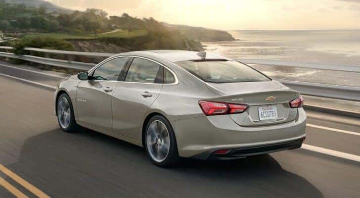 A silver 2023 Chevy Malibu is shown driving to view used cars for sale.