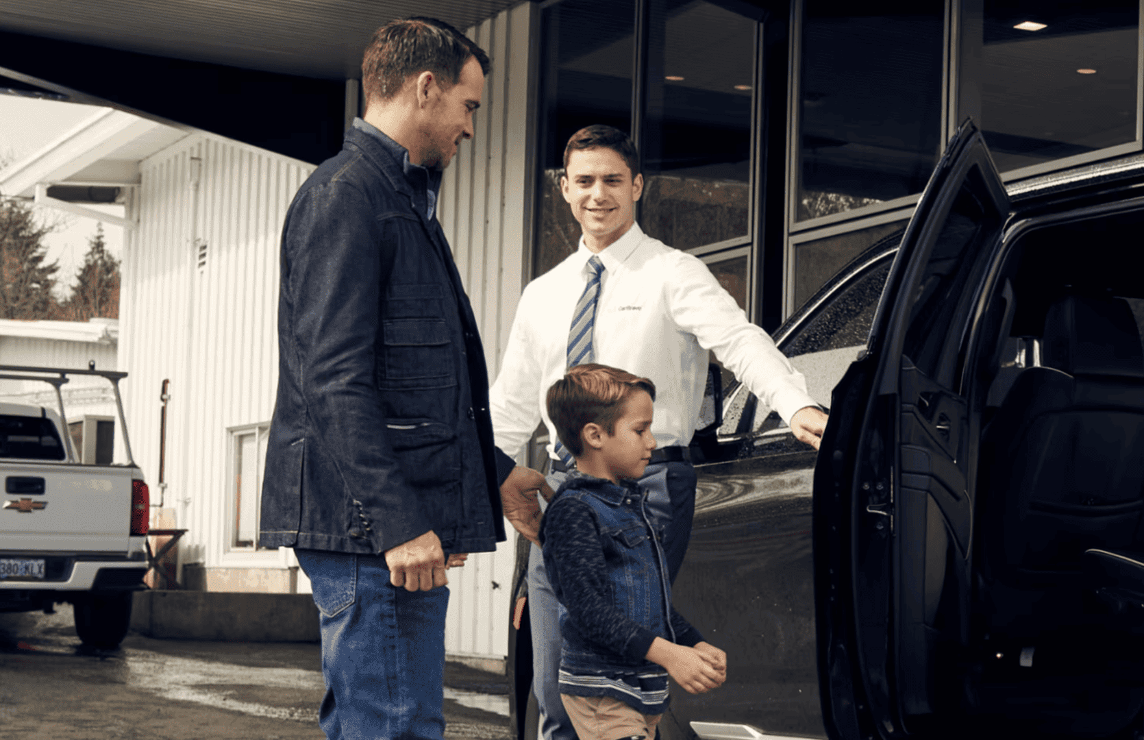 Father and child with dealership staff near a Chevy Certified Pre-Owned vehicle, ready to enter