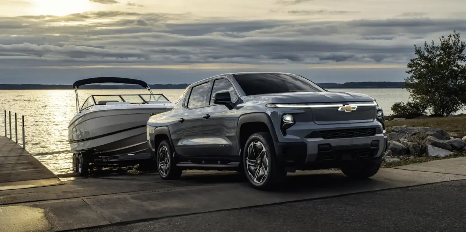 2026 Chevrolet Silverado EV towing a boat at a lakeside launch ramp, showing its 12,500-pound max towing capability