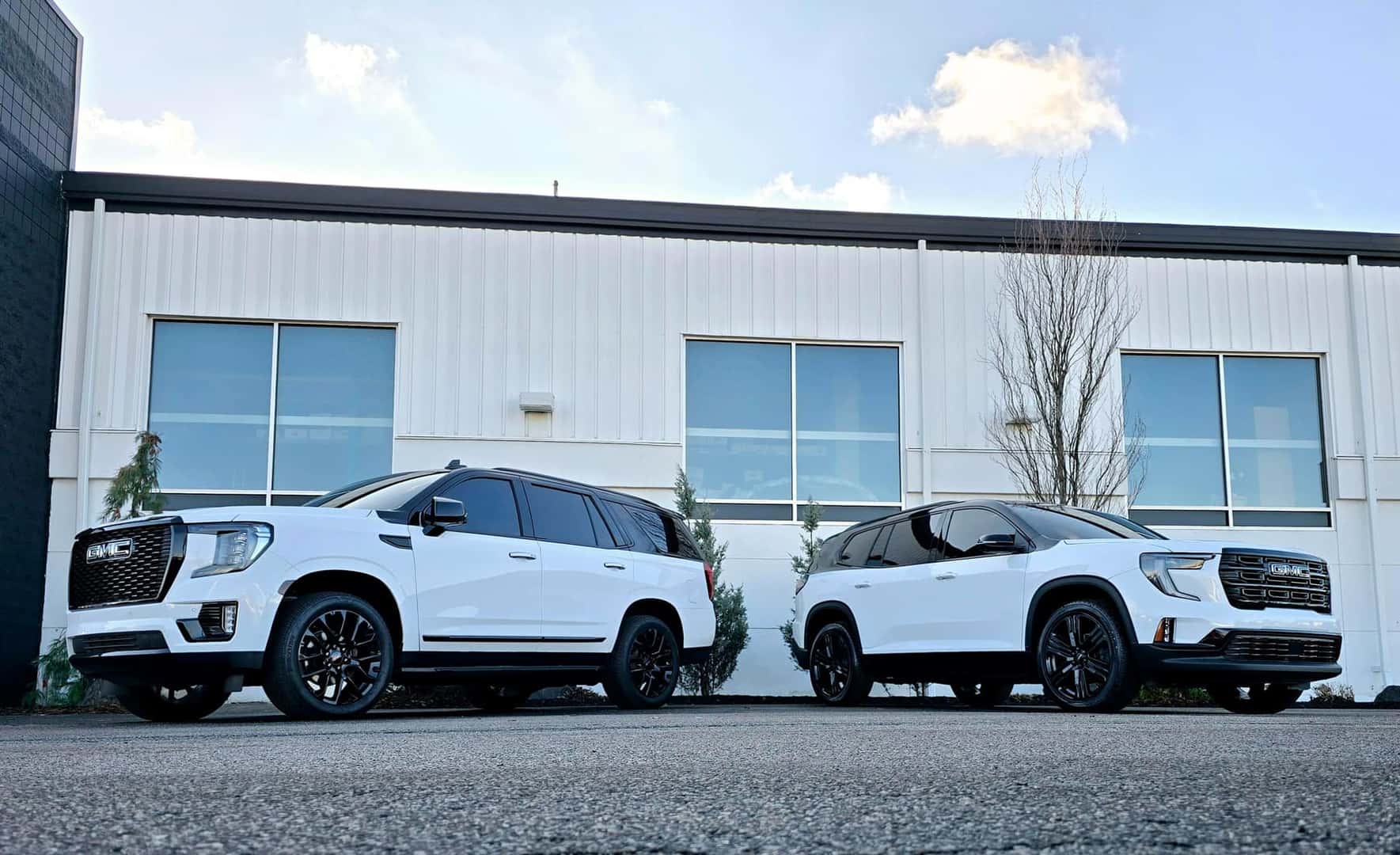 2 White denali vehicles in front of body shop