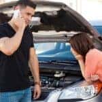 A couple standing near their broken down car, calling OnStar for help
