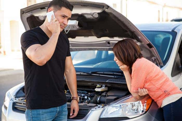 A couple standing near their broken down car, calling OnStar for help